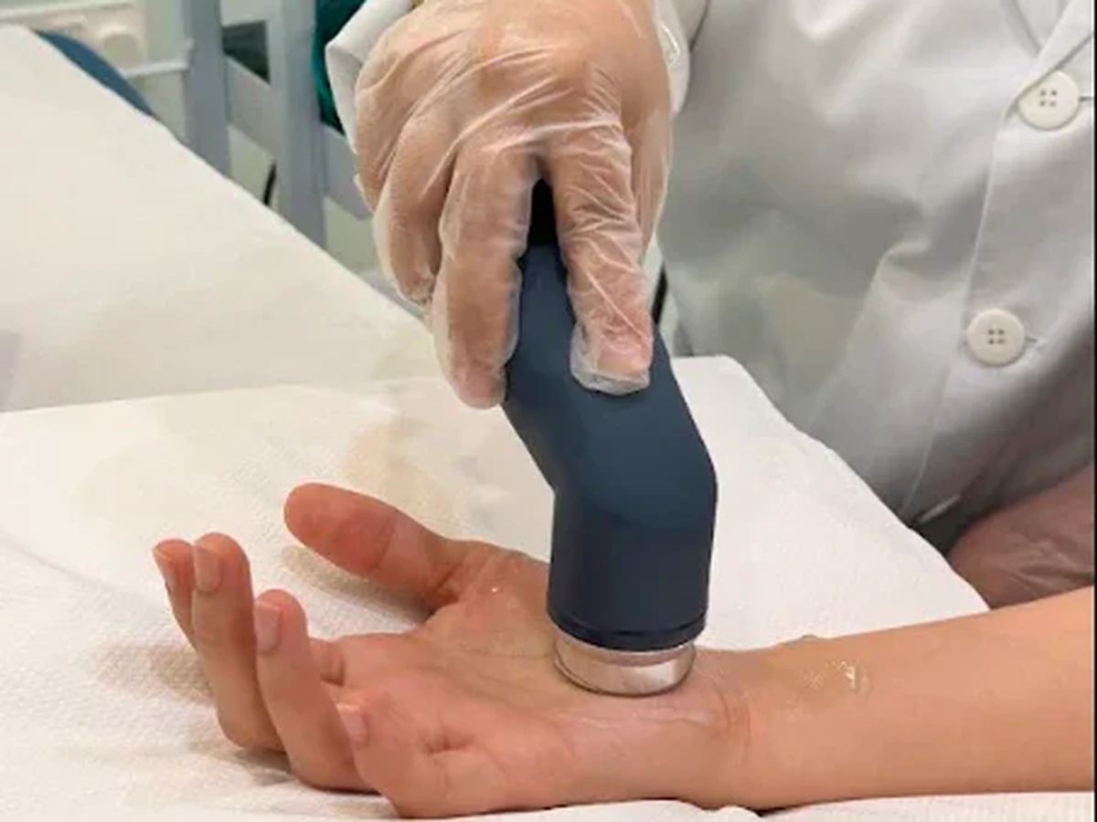 Physiotherapist applying ultrasound therapy to a patient's wrist and palm with a handheld transducer at Physio Care Dubai